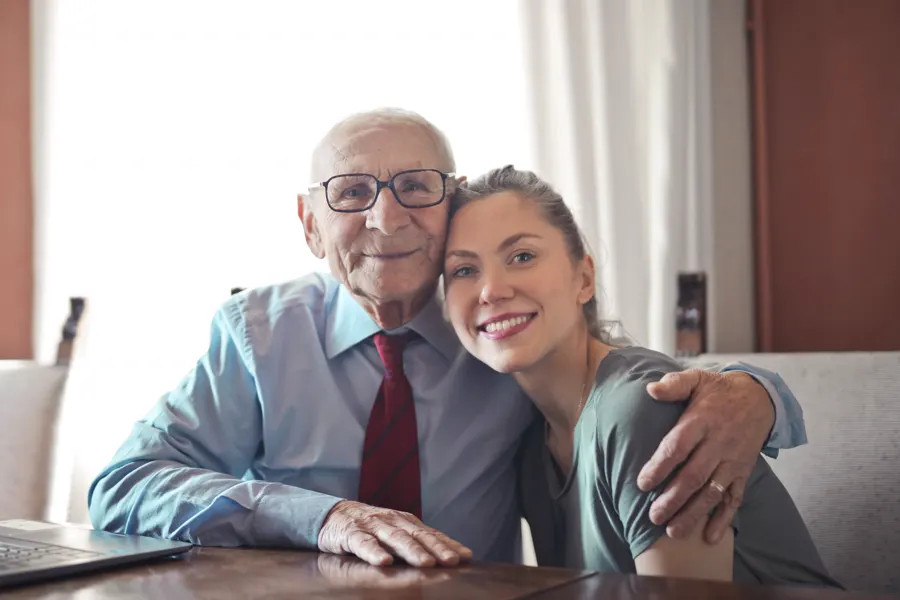 A smiling caregiver hugging an elderly man at home